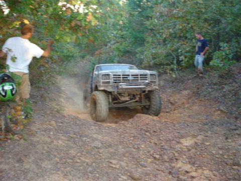 2008 International School Bus - A lifted pickup truck navigates a challenging off-road trail, kicking up dust as it climbs.