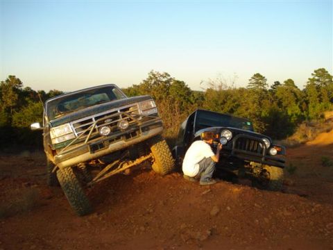2008 International School Bus - A person photographs a black Jeep Wrangler next to a green Ford F-Series truck on a dirt trail.