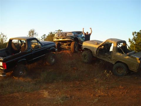 2008 International School Bus - Three trucks are parked on a dirt incline under a clear sky. One truck is black, another is tan and stripped down, and the third is dark gr…