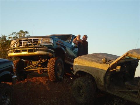 2008 International School Bus - Two modified trucks are positioned on a dirt mound under a clear sky, with one truck's hood open.