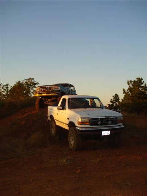 2008 International School Bus - Two pickup trucks are positioned on a dirt incline against a clear sky at sunset.