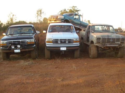 2008 International School Bus - Several trucks and an SUV are parked together on a dirt surface, with one truck elevated behind the others.
