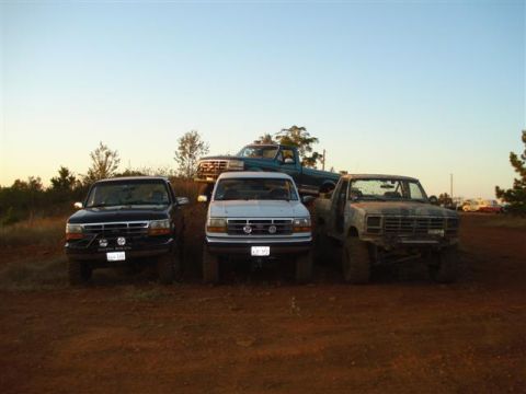 2008 International School Bus - Several pickup trucks are parked on a dirt incline under a clear sky.