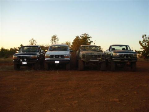 2008 International School Bus - Four pickup trucks are parked in a dirt area with trees in the background under a clear sky.