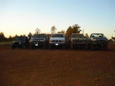 2008 International School Bus - A collection of modified trucks and a Jeep are parked in a dusty outdoor area.