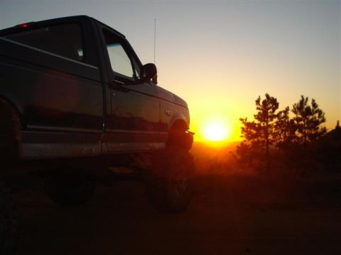 2008 International School Bus - A pickup truck is silhouetted against a vibrant sunset, with trees and hills in the distance.