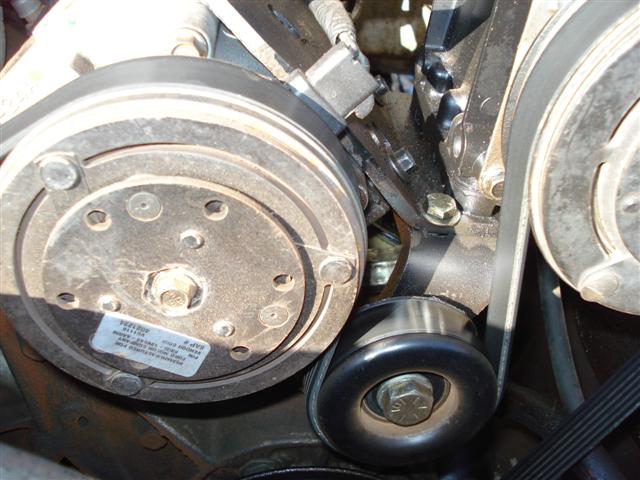 close-up of engine belt tensioner and AC compressor with a label on the compressor