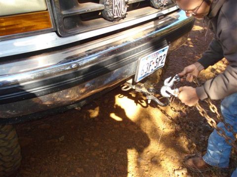 2008 International School Bus - A person attaches a tow chain to the front bumper of a truck.