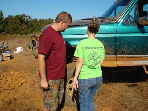 2008 International School Bus - A teal truck, likely from the 1990s, is covered in mud as two people stand next to it.