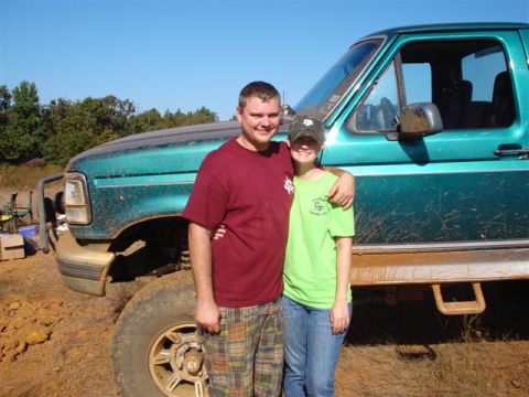 2008 International School Bus - Couple poses in front of a muddy, lifted pickup truck on a sunny day.