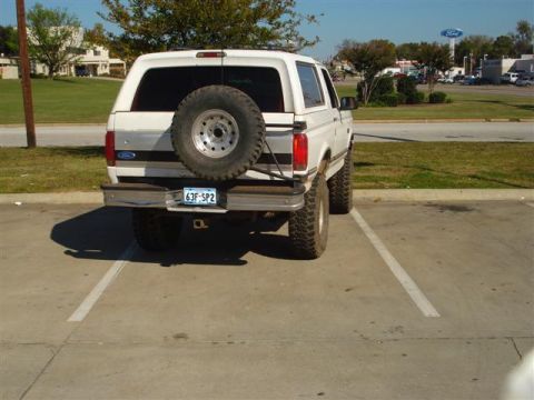 2008 International School Bus - This lifted white Ford Bronco is parked in a lot, showing its rear end and spare tire.