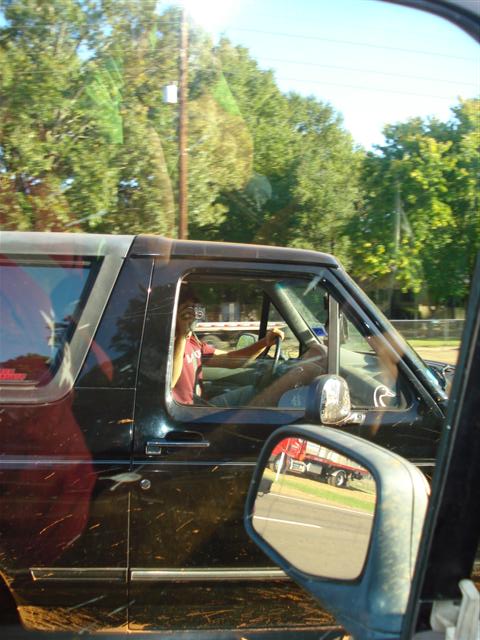 2008 International School Bus - A black SUV is seen from the side, with a driver behind the wheel. A red truck is visible in the side mirror.