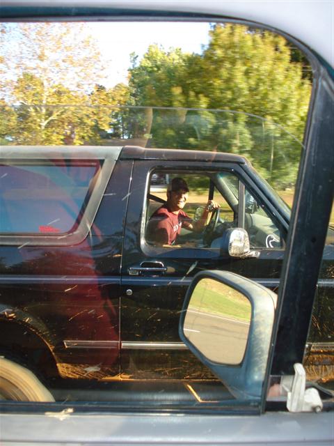 2008 International School Bus - A driver smiles from inside a muddy black SUV, seen from another vehicle.