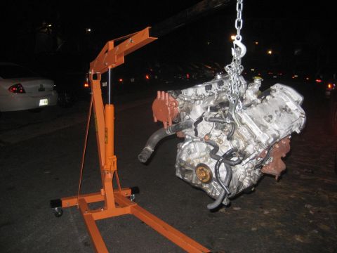 1993 Ford Probe - An engine is suspended by chains from an engine hoist, with a car visible in the background.