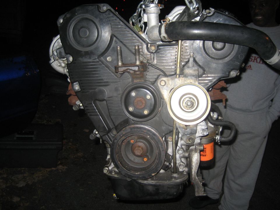 Engine assembly with black timing cover and orange oil filter. Being lifted by chains