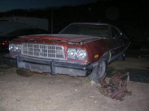 1975 Ford Ranchero - A brown 1975 Ford Ranchero sits with its hood ajar, showing a damaged grille and front end.
