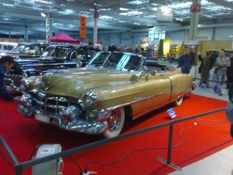 1991 Ford Crown Victoria - A classic gold Cadillac convertible is displayed indoors at a car show.