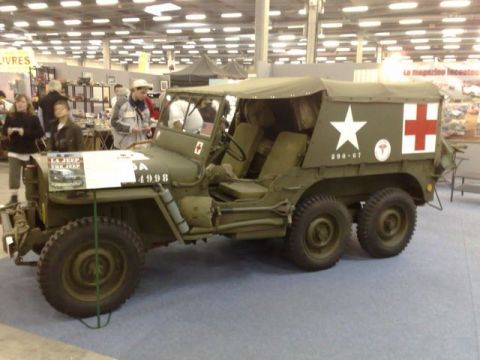 1991 Ford Crown Victoria - This six-wheeled military ambulance, marked with a white star and red cross, is displayed indoors at an indoor event.