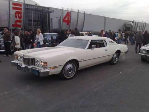 1991 Ford Crown Victoria - White 1977 Ford Thunderbird coupe at an outdoor event with a crowd in the background.