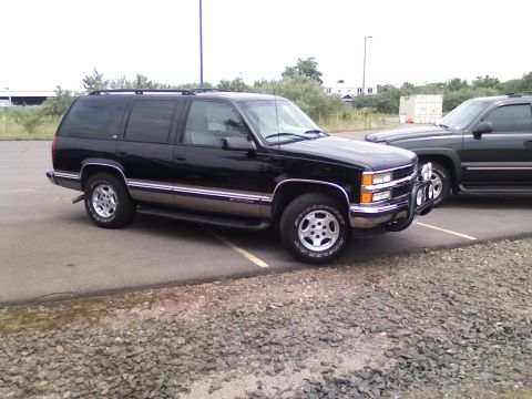 1998 Chevrolet Tahoe - A black Chevrolet Suburban is parked in a lot, with another vehicle visible behind it.