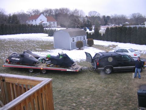 1998 Chevrolet Tahoe - Two snowmobiles are loaded onto a trailer, hitched to a black SUV in a snowy yard.