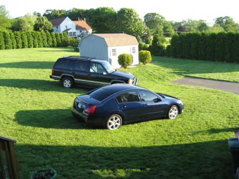 1998 Chevrolet Tahoe - Two vehicles are parked on a lawn in front of a residential house and a shed.