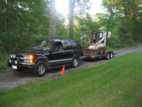 1998 Chevrolet Tahoe - A black 1998 Chevrolet Tahoe tows a trailer carrying a skid steer loader on a wooded dirt road.