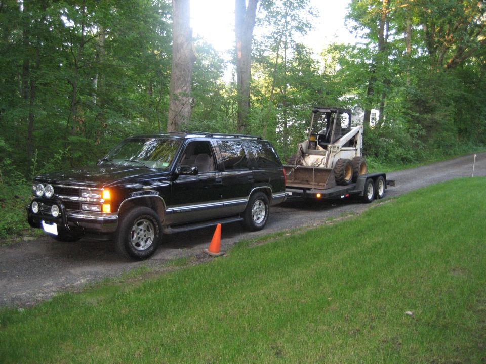 Black 1998 Chevrolet Tahoe towing a trailer with a skid steer loader on a dirt road