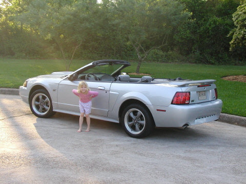 2002 Ford Mustang - A young girl poses next to a silver convertible Mustang on a sunny day.