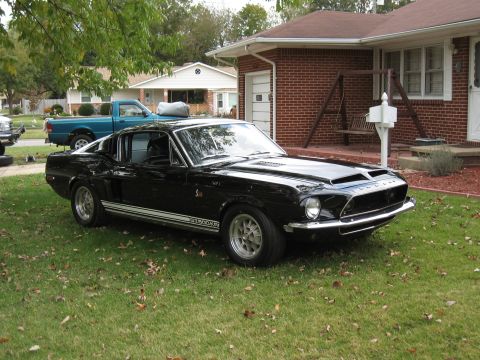 1968 Shelby GT500 - A black 1968 Shelby GT500 is parked on a grassy lawn next to a brick house.