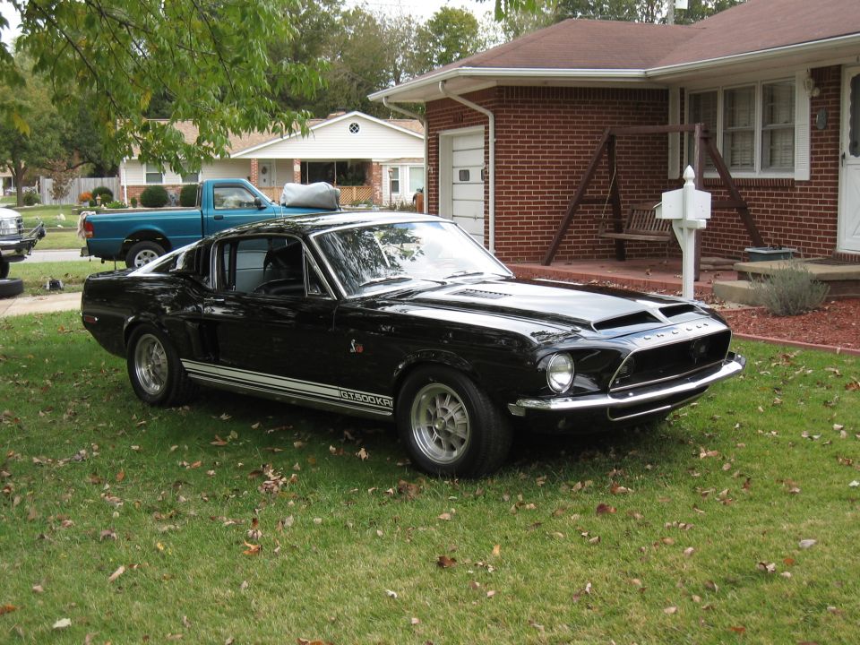 Black 1968 Shelby GT500 parked on a lawn in front of a brick house