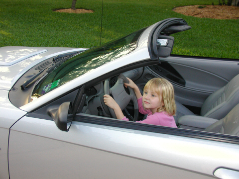 2002 Ford Mustang - A young girl pretends to drive a silver convertible, identified as a 2002 Ford Mustang.