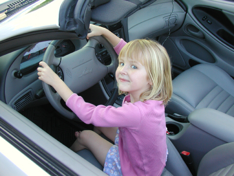 2002 Ford Mustang - Young girl pretends to drive a 2002 Ford Mustang, holding the steering wheel.