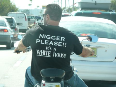 1995 Dodge 1500 - A man rides a motorcycle through traffic while wearing a t-shirt with offensive text.