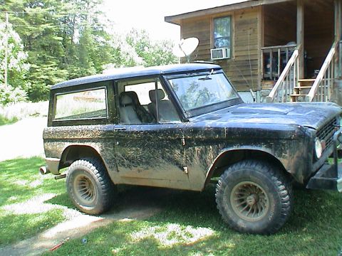 1972 Ford Bronco - Mud-covered 1972 Ford Bronco parked in front of a wooden house.