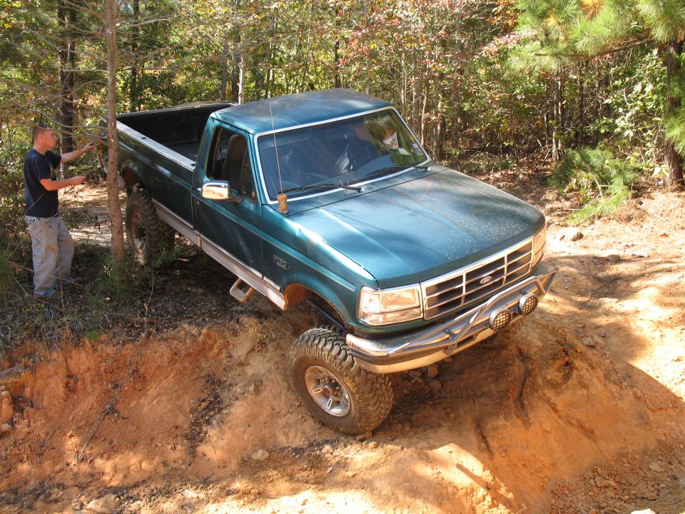 Green lifted Ford F-250 pickup descending a steep dirt embankment in the woods
