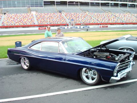 1977 Ford F-100 - A custom coupe sits on display at a racetrack with spectators nearby and the hood raised to show the engine.