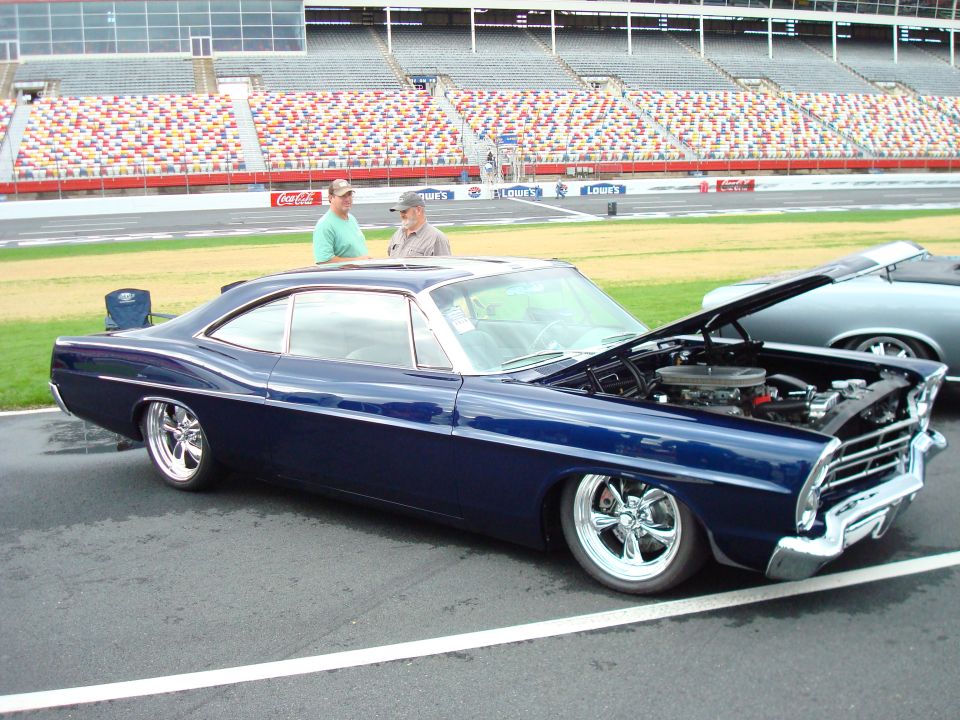 dark blue coupe with hood open, parked next to another car at a racetrack