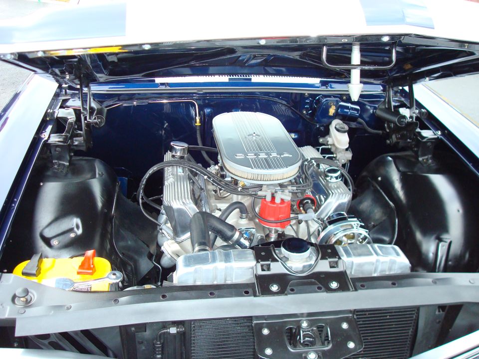 Engine bay of a blue vehicle with a chrome air cleaner and V8 engine. A yellow battery is visible