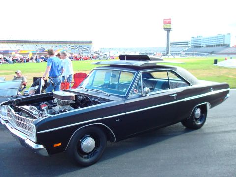 1977 Ford F-100 - A black 1967 Dodge Dart Swinger is displayed with its hood open, revealing the engine, and features a prominent roof scoop.