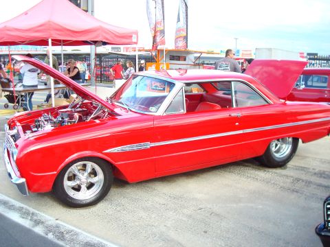 1977 Ford F-100 - A red 1963 Ford Falcon coupe is displayed with its hood open at an event.