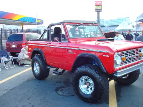 1977 Ford F-100 - A red Ford Bronco is parked next to a red SUV, with a gas station canopy in the background.