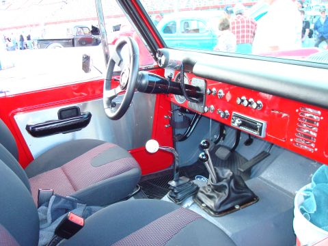1977 Ford F-100 - The interior of a red vehicle features a dashboard with an aftermarket radio, manual shifters, and two rows of seats.