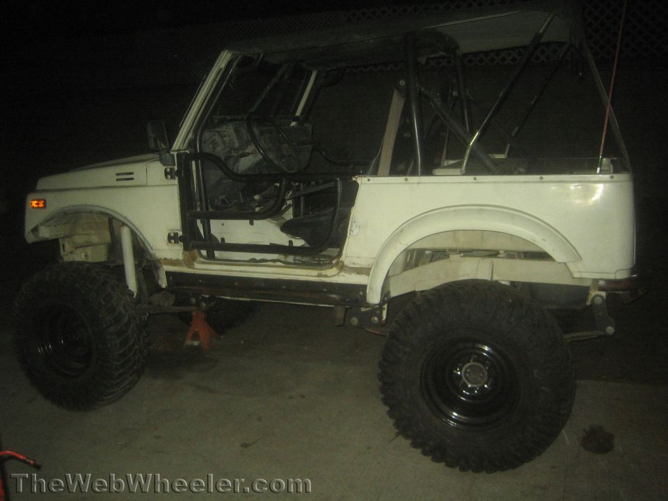 White off-road SUV with roll cage, large tires, and no doors. It's on jack stands
