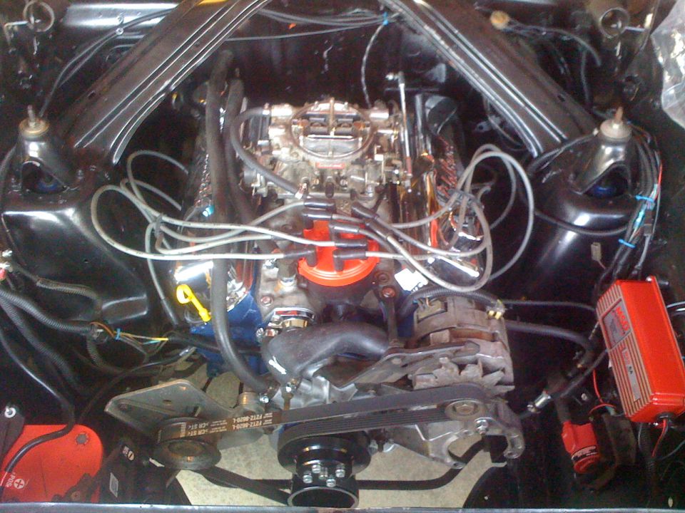 Engine bay showing V8 engine, carburetor, distributor, alternator, and red ignition box