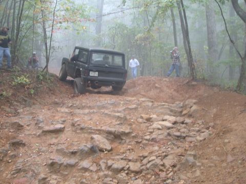 1972 Ford Bronco - An off-road vehicle navigates a challenging, rocky path through a misty forest.