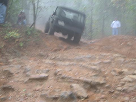1972 Ford Bronco - A black SUV navigates a challenging off-road trail with trees and fog in the background.