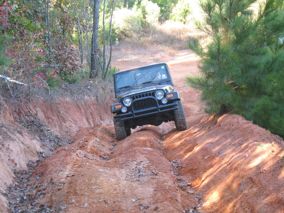 Black Jeep Wrangler driving down a rutted red-dirt forest trail