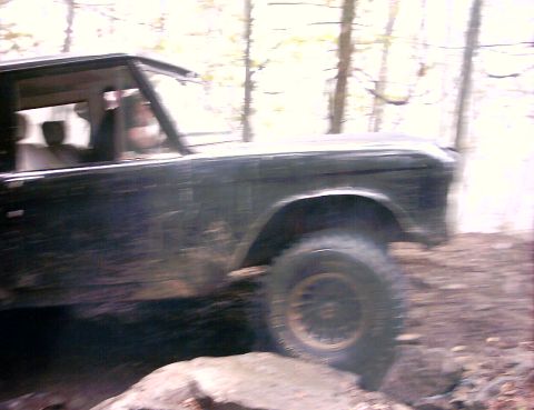 1972 Ford Bronco - A black Ford Bronco navigates a rocky, wooded trail, captured from the side.