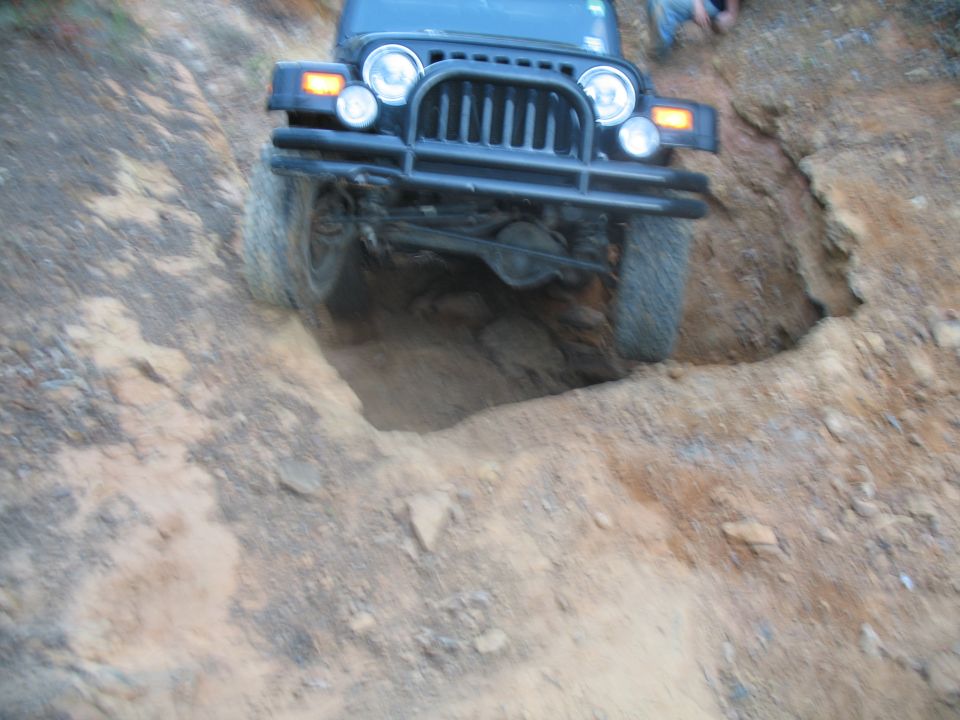 Front of a black Jeep Wrangler dropping into a deep dirt hole off-road